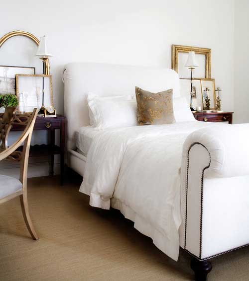 Gold frames leaning on nightstands in a bedroom with white upholstered bed 