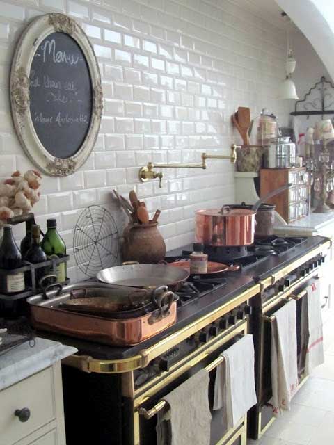 Black stove with gold accents in a kitchen with white subway tile and copper pots