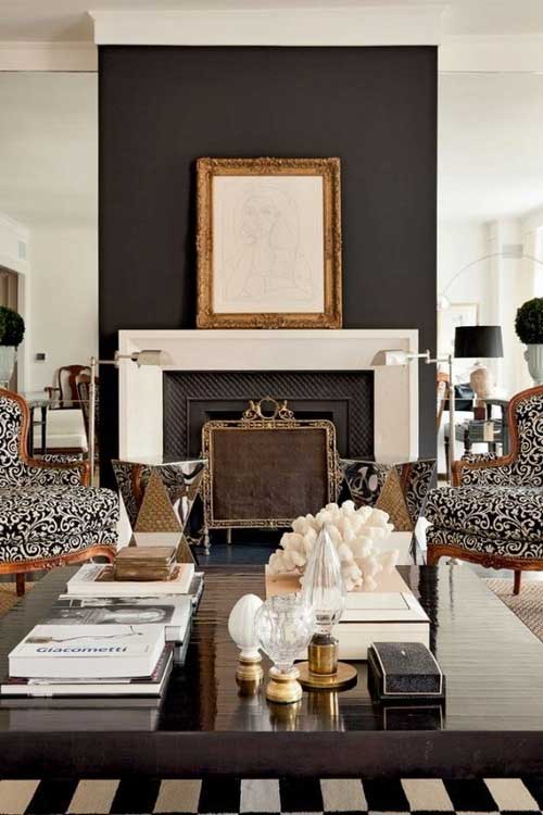 Modern room with black painted wall behind the fireplace and gold framed art on mantel