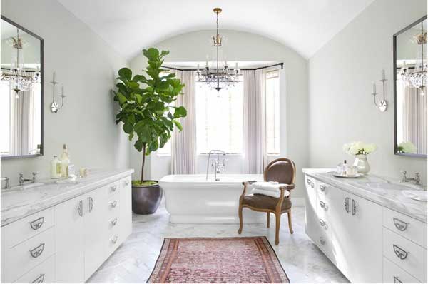 White marble bathroom with window behind freestanding tub and large fiddle leaf fig in corner