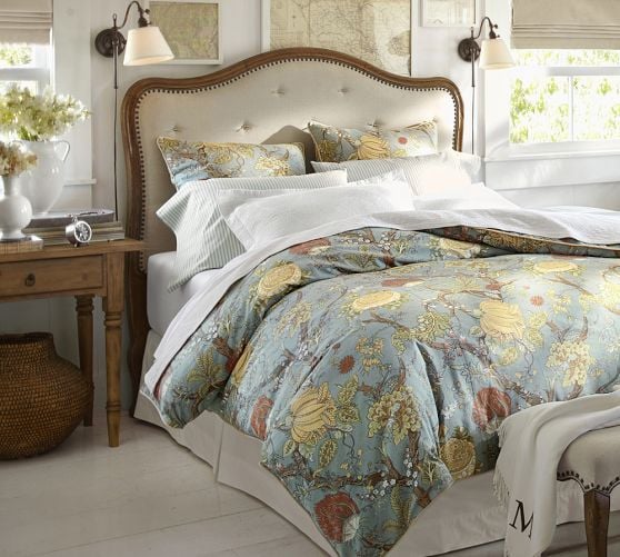 Bedroom with tufted headboard with floral bedding and two plug-in sconces on sides of bed