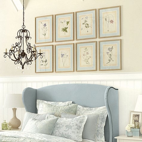 Bedroom with blue wingback bed and eight flower prints hanging on the wall above