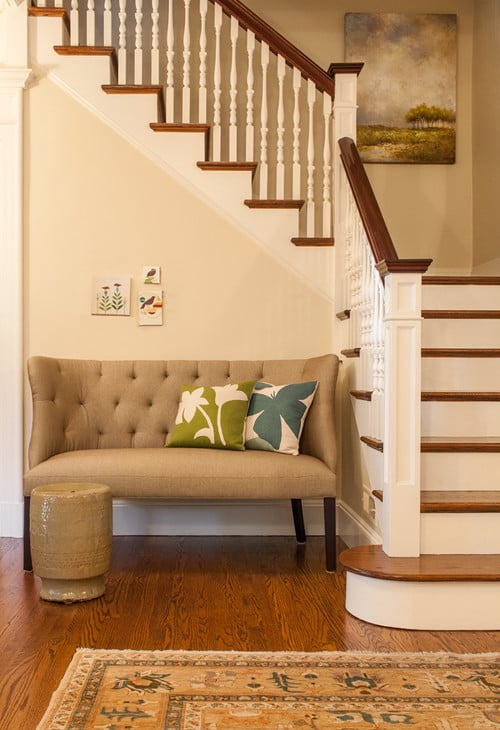 Foyer with small beige tufted settee at the bottom of the stairs