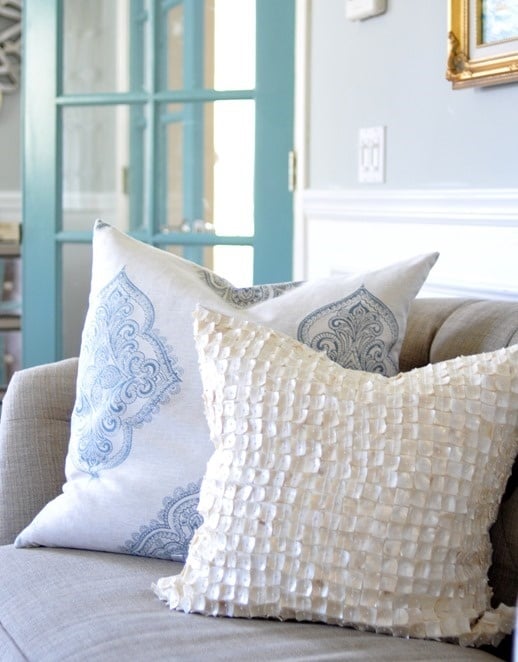 Closeup of two pillows on a beige sofa one pillow is blue and white and one is a white seashell pillow