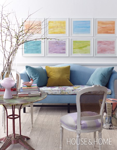 Blue velvet sofa with pink and yellow floral seat and pastel artwork hanging on the wall above