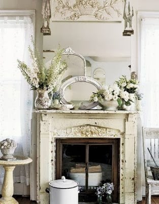 Antique white fireplace with a collection of mirrors and flowers on the mantel