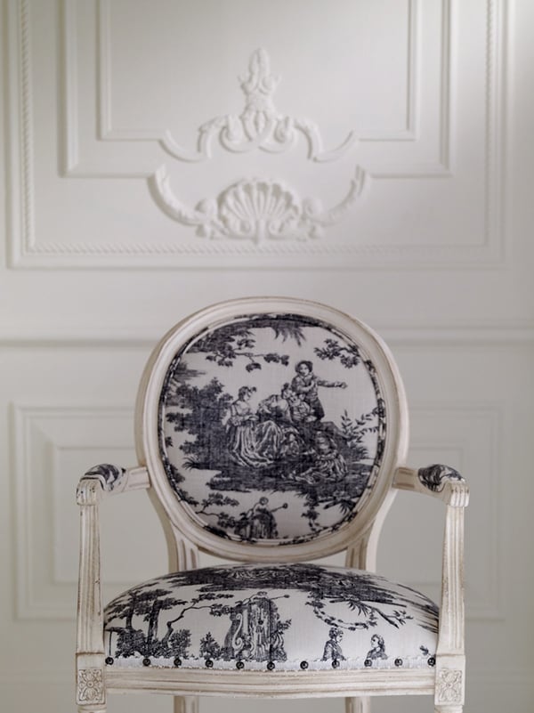 closeup of black and white toile upholstered french chair with white wall trimmed with molding