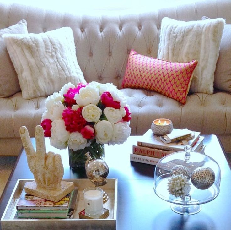 Coffee table with items in each of the four corner pink and white flowers and tufted sofa