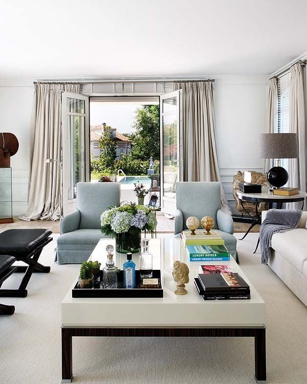 Contemporary living room with white coffee table blue accent chairs and french doors open to pool