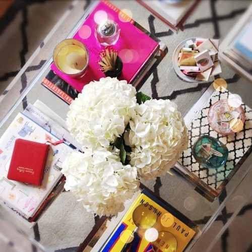 Lucite coffee table with books in all corners and white hydrangeas in the center