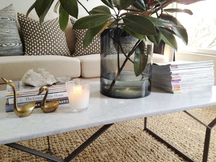 Marble coffee table with vase of magnolia leaves on top and stacks of magazines