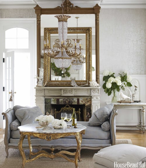 elegant french living room with two gold mirrors above fireplace and blue settee