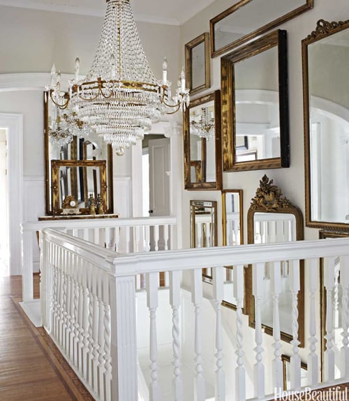 top of a white staircase with wall full of antique gold mirrors and large gold and crystal french chandelier hanging above