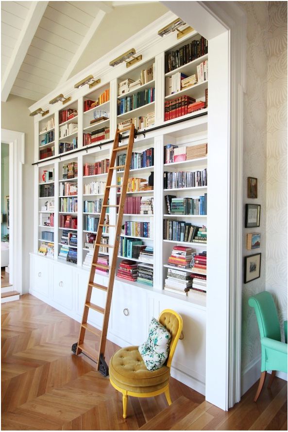 white floor to ceiling bookshelves with bronze lights and wood library ladder rolling