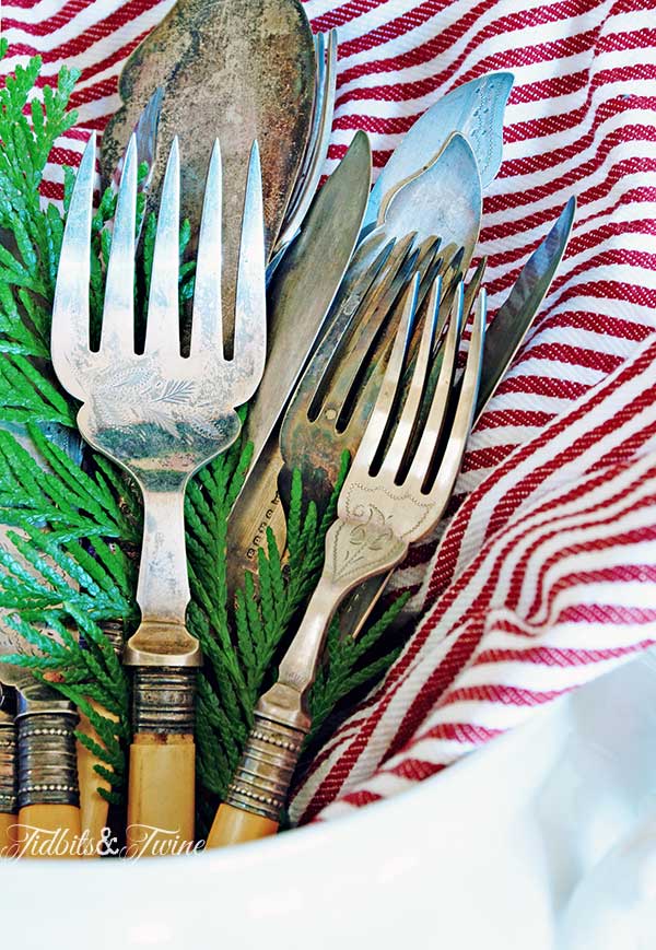 White ironstone with red and white striped napkin holding vintage flatware and holiday greenery