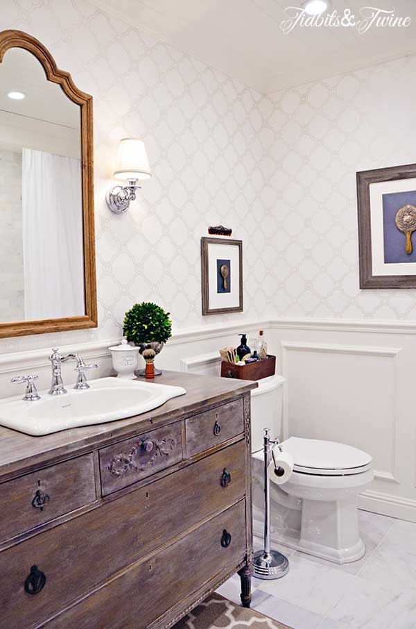 A guest bathroom transformation: from builder-grade to beautiful! Beadboard ceiling, wallpaper, sconces, marble floors, and a vanity converted from a vintage dresser!