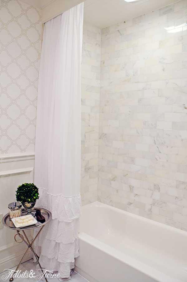 marble subway tile tub shower surround with white ruffle shower curtain and silver tray table next to tub