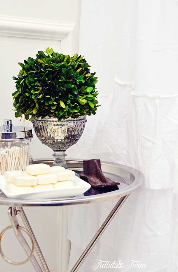 Closeup of silver butler tray in bathroom with small soaps and Q-tips on top and preserved boxwood ball