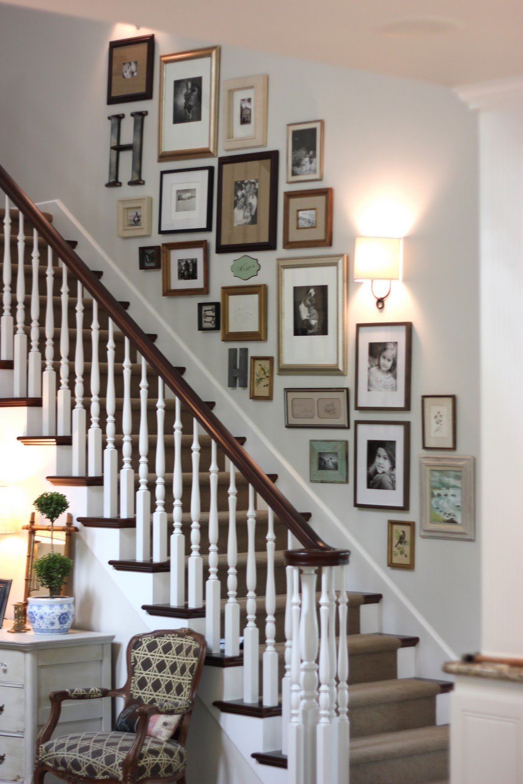 Electic gallery wall stairway decor featuring family photos and a wall sconce with white railing