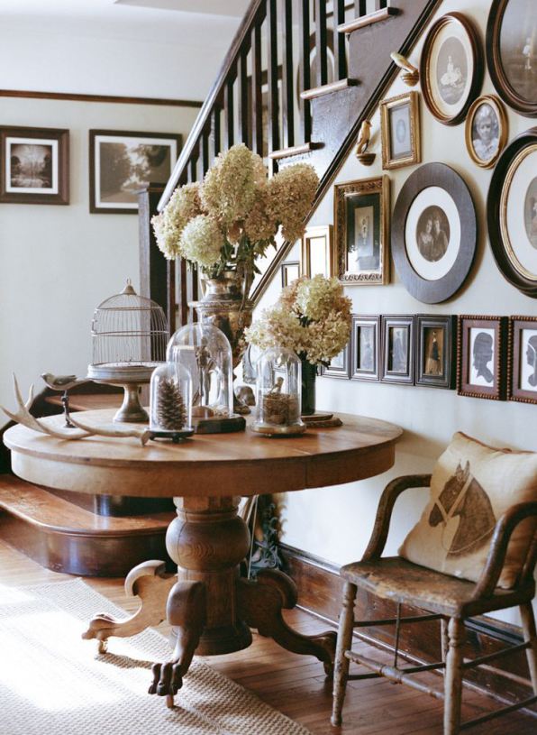 eclectic gallery wall on staircase with antique gold and black frames and round table at the bottom with dried hydrangeas