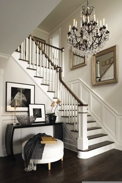 white staircase with dark wood floors and large crystal and iron chandelier and two large mirrors on wall