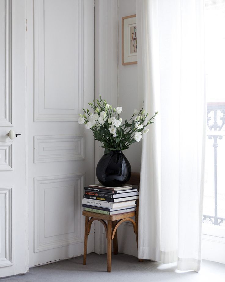 small antique chair in a parisian apartment corner stacked with books and topped with a black vase holding white flowers