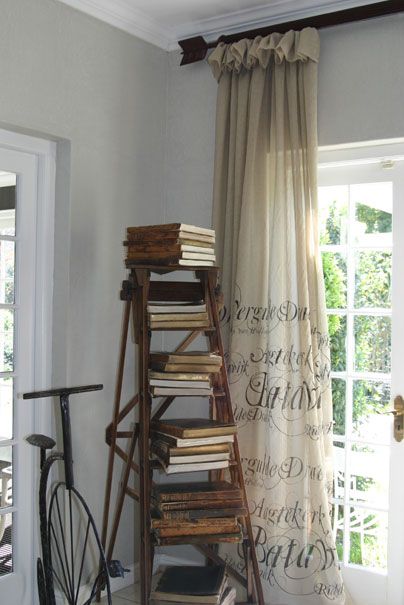 rustic ladder in an empty living room corner stacked with antique books and drapery with antique writing on it