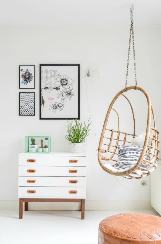 rattan egg swing hanging from ceiling of empty bedroom corner next to white modern set of drawers