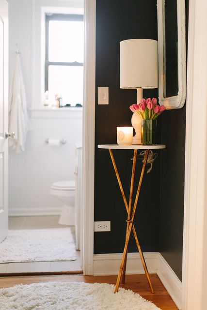 small gold three legged side table filling the corner of a room topped with a lampa nd flowers