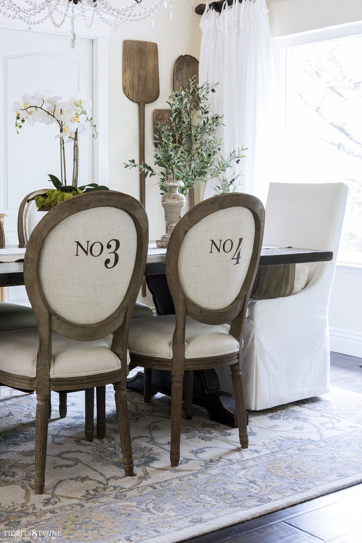 dining room with french chairs with numbers on the back and white velvet head chairs at trestle table