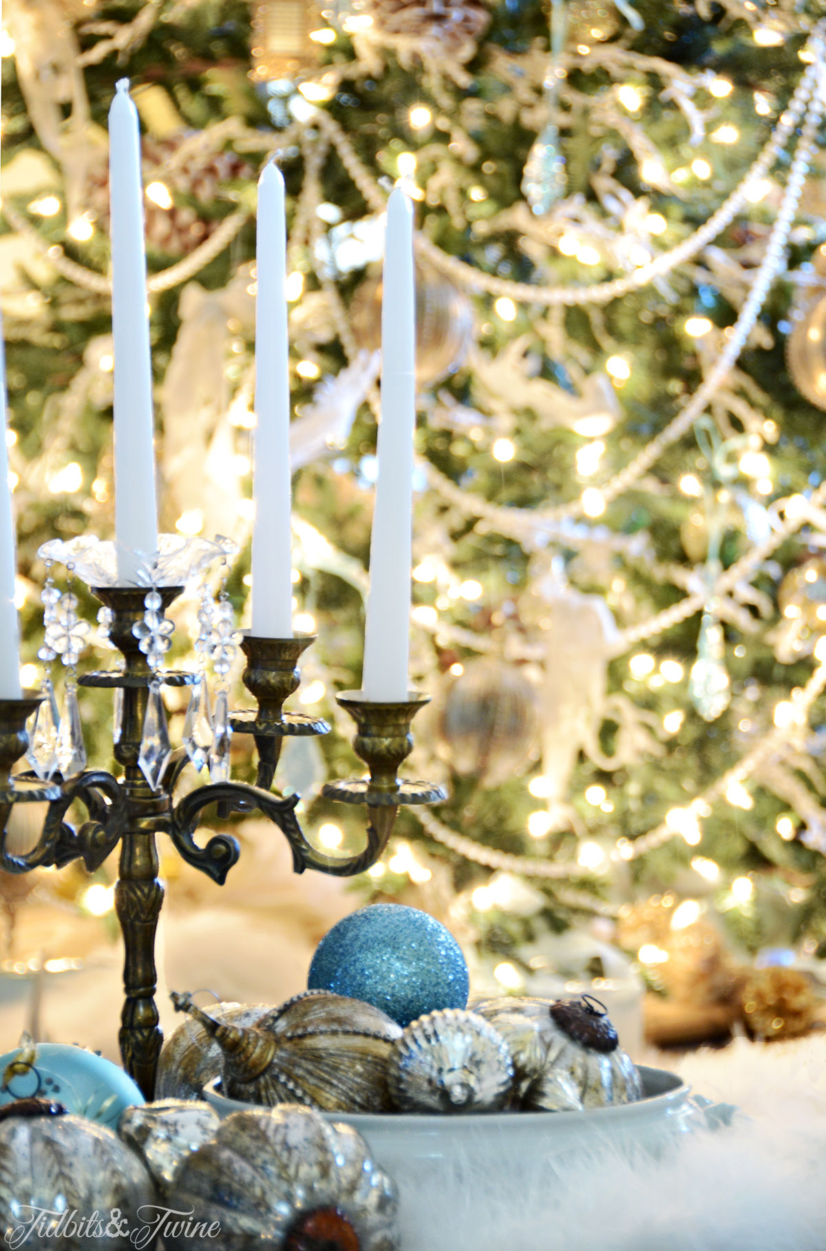 Gold candelabra next to ironstone bowl full of ornaments with Christmas tree in the background