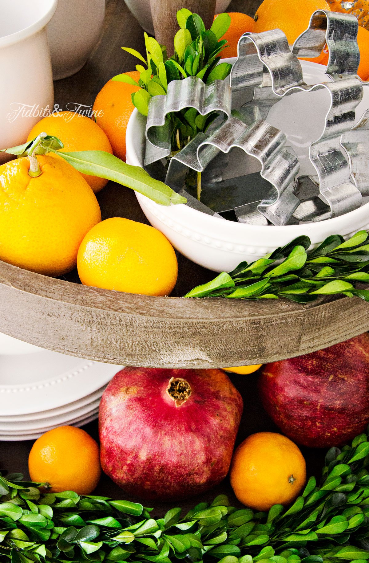 Tiered wooden kitchen tray filled with Christmas cookie cutters fruit and boxwood garland