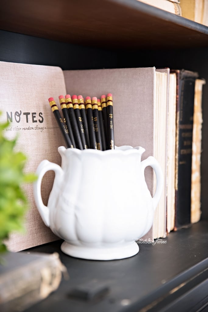 white vintage ironstone sugar jar holding black pencils with antique books propped up next to it