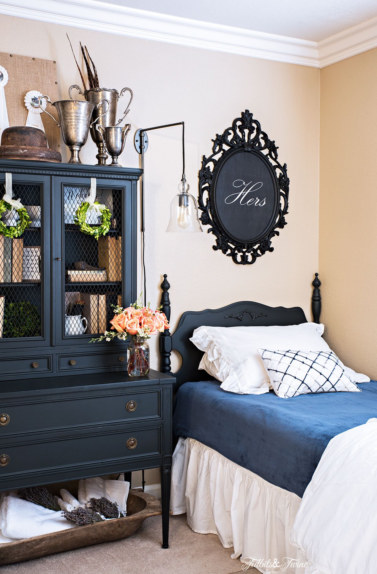 black antique bed with blue and white bedding and black artwork above and black antique hutch with books and trophies