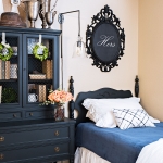 black antique bed with blue and white bedding and black artwork above and black antique hutch with books and trophies