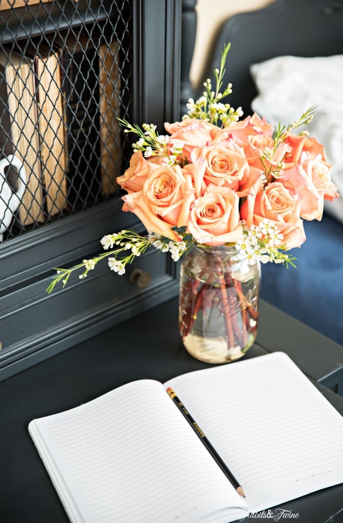 mason jar of peach roses on black antique hutch in bedroom with bed in background blue blanket