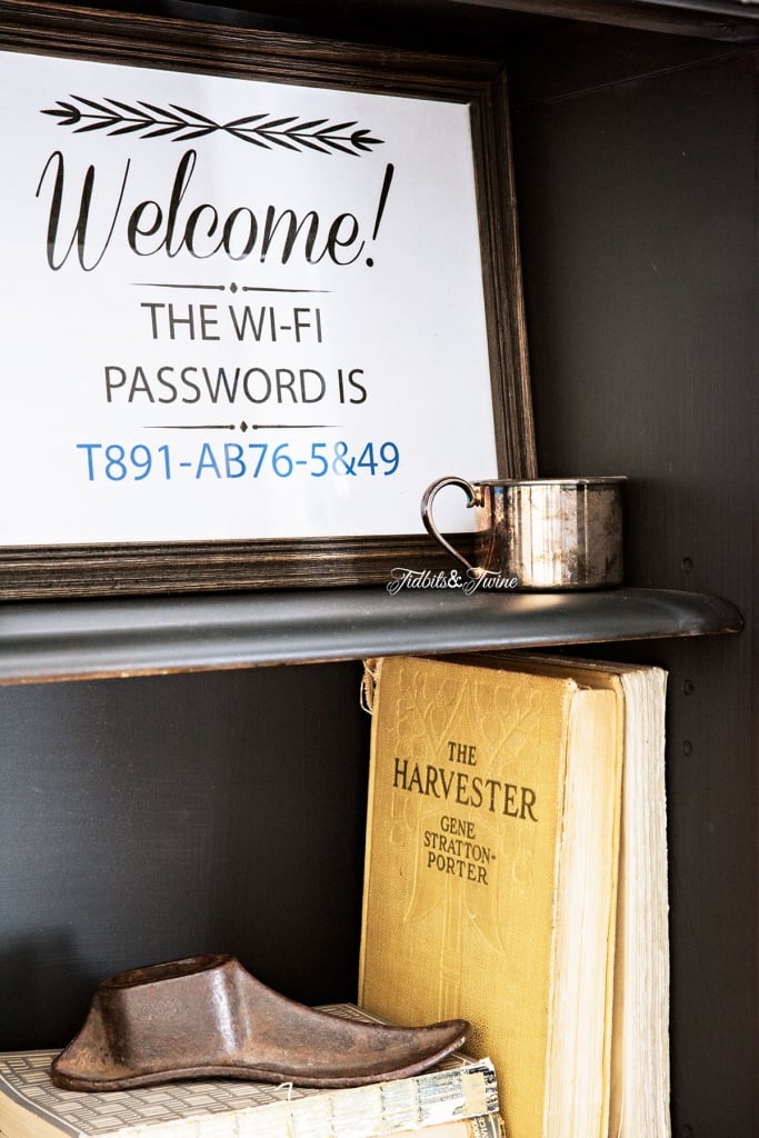 interior of black antique hutch with printable sign with the wi-fi password in a brown frame with silver cup in front and books below