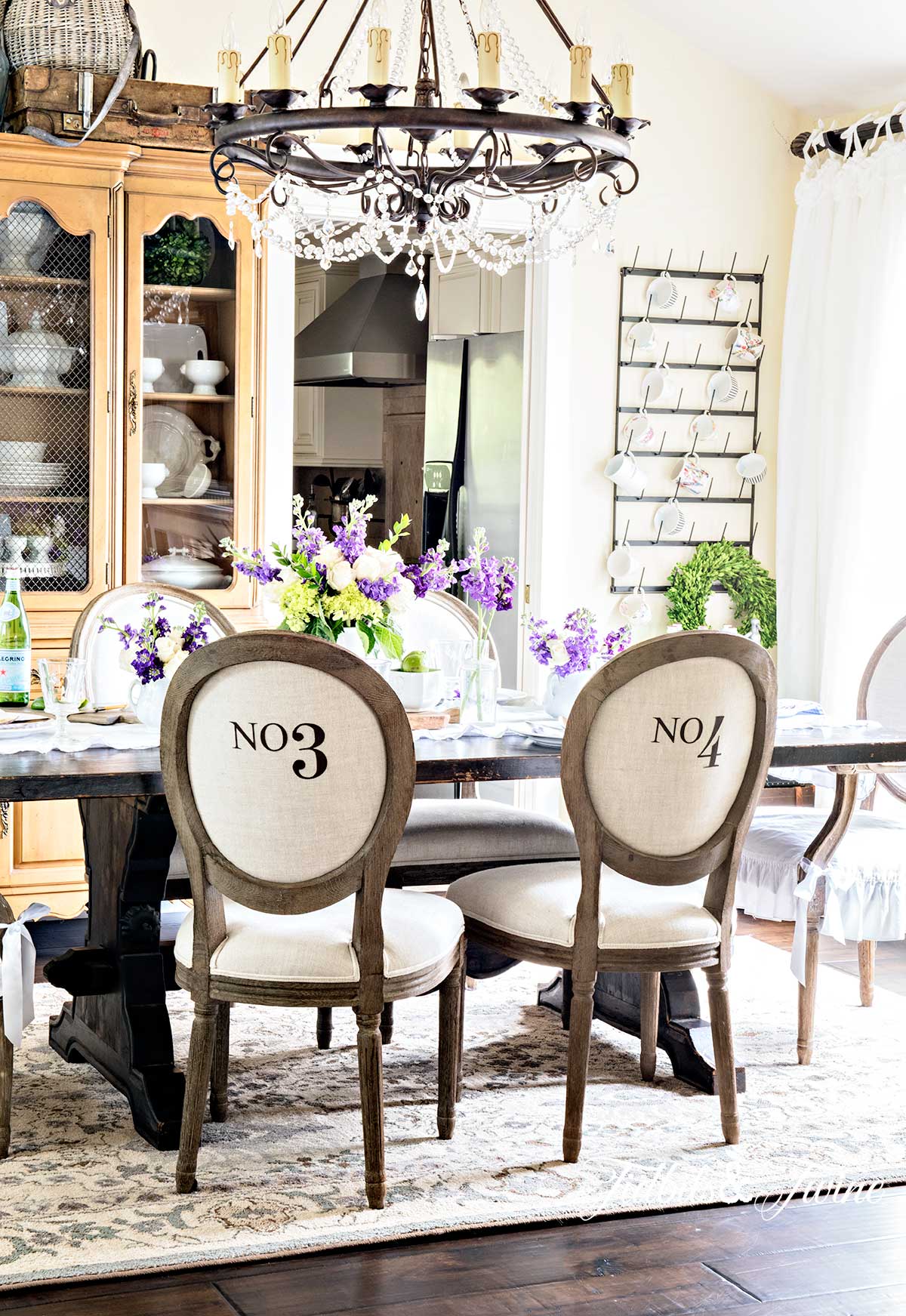 A French country dining room with numbered chairs a crystal chandelier and antique dining hutch