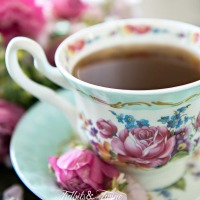 turquoise and pink antique teacup filled with coffee with pink flowers in the saucer and pink flowers in background