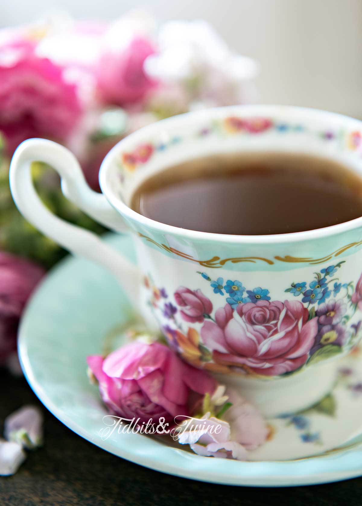 turquoise and pink antique teacup filled with coffee with pink flowers in the saucer and pink flowers in background