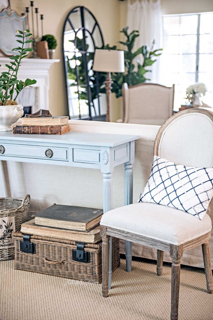 blue french sofa table with french linen chair on the side with baskets and books underneath and french wingback chair in background