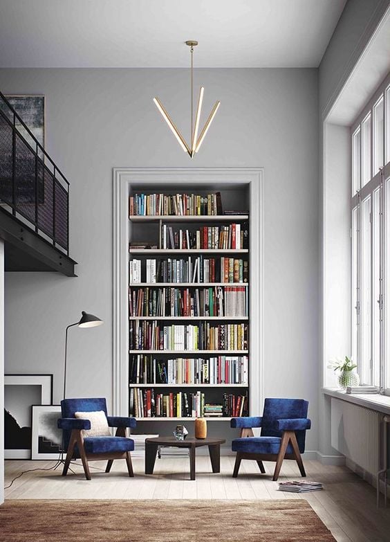 Tall recessed bookcase filled with books in a gray living room with blue chairs