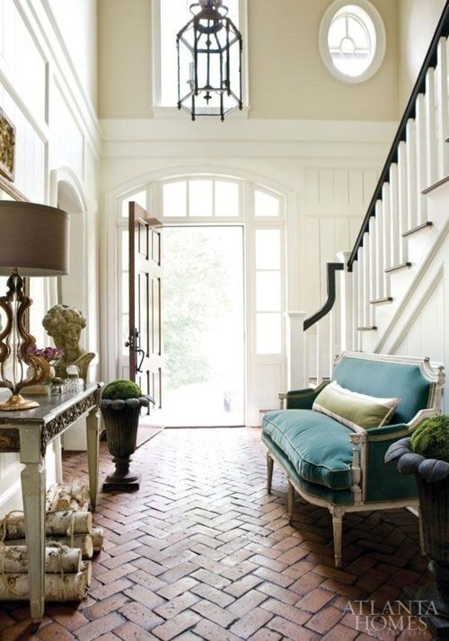 Two story foyer with herringbone brick floor and blue velvet settee