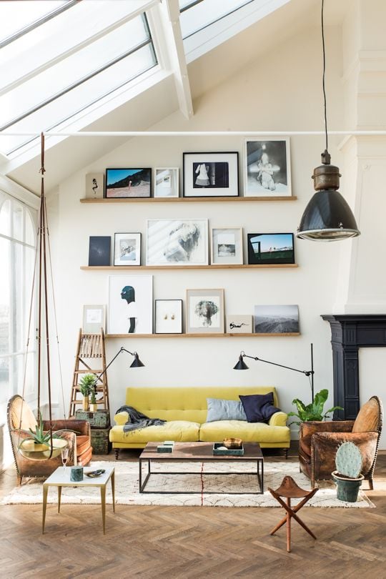 Three floating shelves holding framed art above a yellow sofa