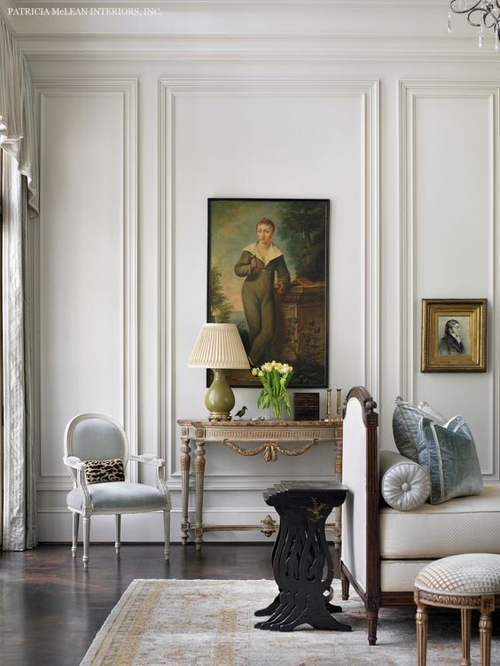 White wall trim on living room walls with vintage artwork a french chair and a settee