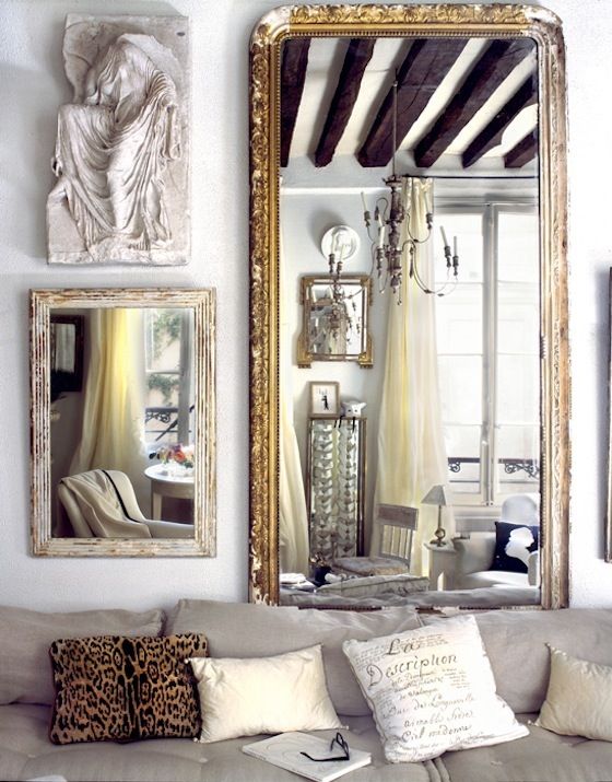 Tall gold antique mirror above a sofa with a small mirror and sculpture next to it on the wall