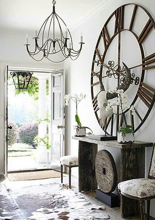 Entryway foyer with cowhide rug and huge clock hanging above console table that holds two orchids