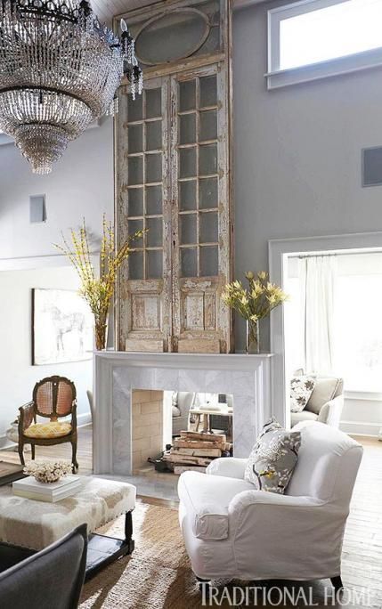 Antique french doors hanging above a white and marble fireplace with a huge crystal chandelier