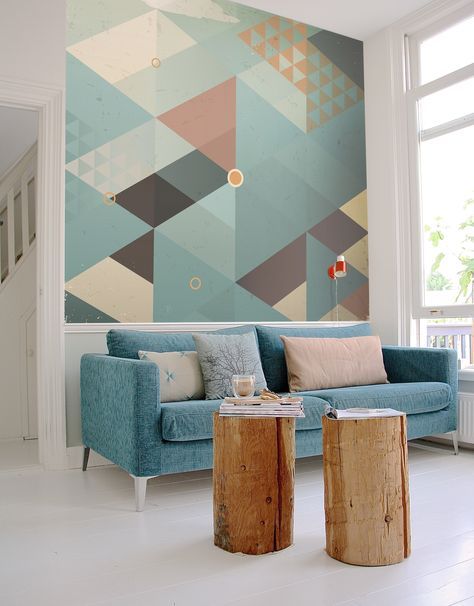 Blue and gray triangle geometric mural above a blue sofa with wood stump coffee table