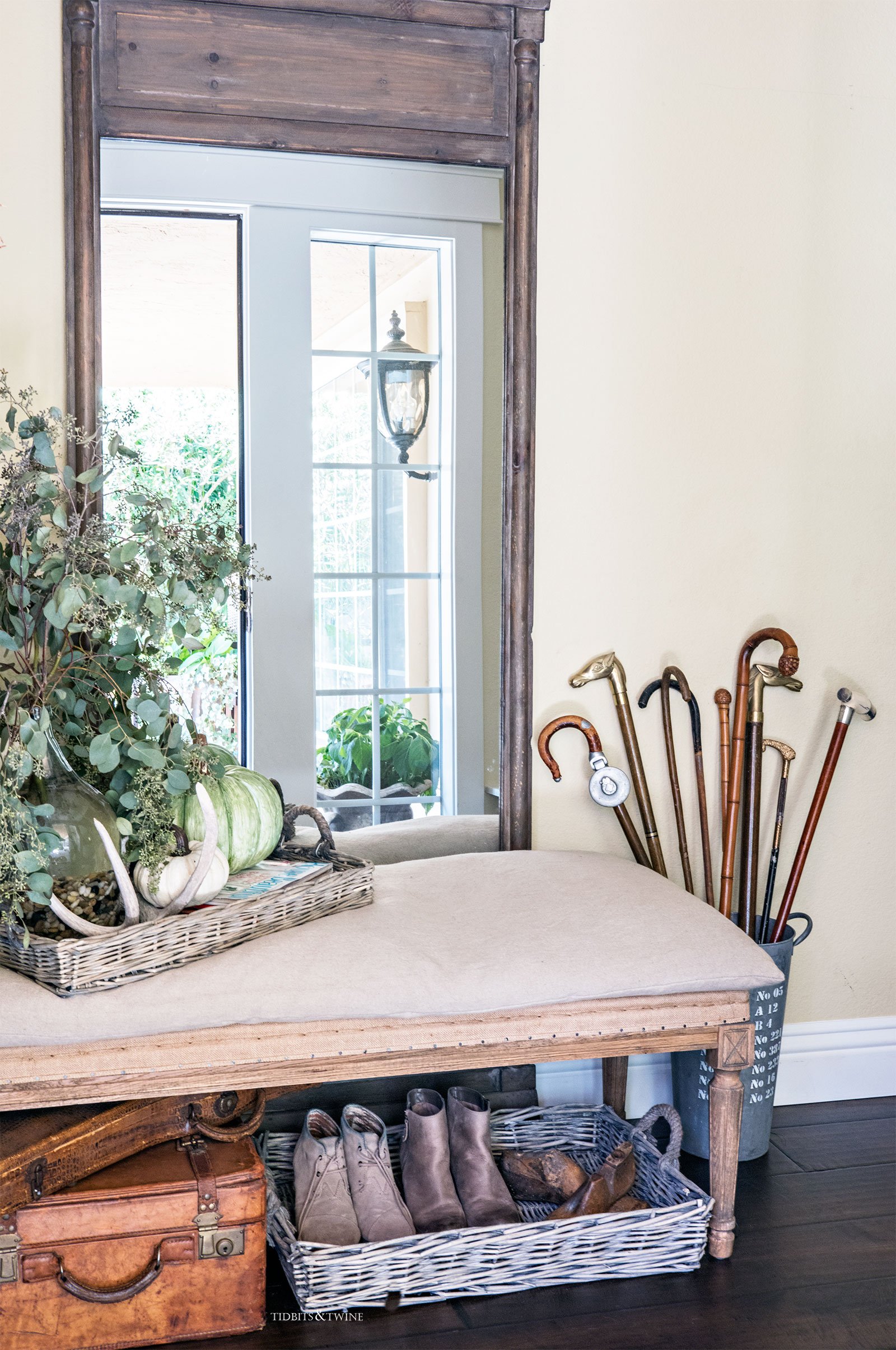 entryway with wooden french mirror and wood and burlap bench eucalyptus and pumpkins and antique cane collection